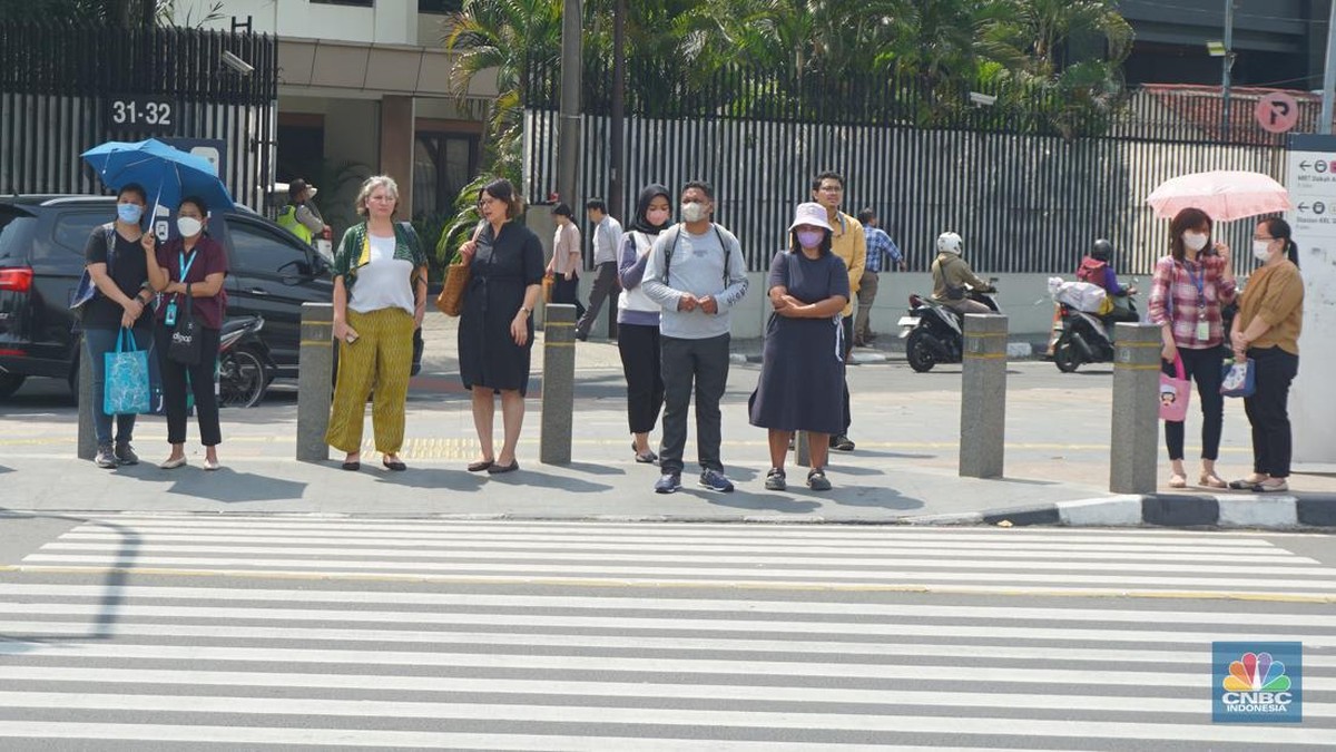 Foto: Pejalan kaki menggunakan payung untuk menghindari terik matahari di kawasan Jembatan Pinisi di halte busway Karet, Jakarta, Selasa (19/12/2023). (CNBC Indonesia/Muhammad Sabki)