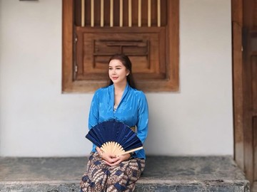 Aura Kasih tampil begitu anggun dan memesona saat mengenakan balutan busana adat Jawa berupa kebaya berwarna biru yang dipadukan dengan kain batik cokelat serta selendang kuning yang terikat rapi di pinggangnya. 