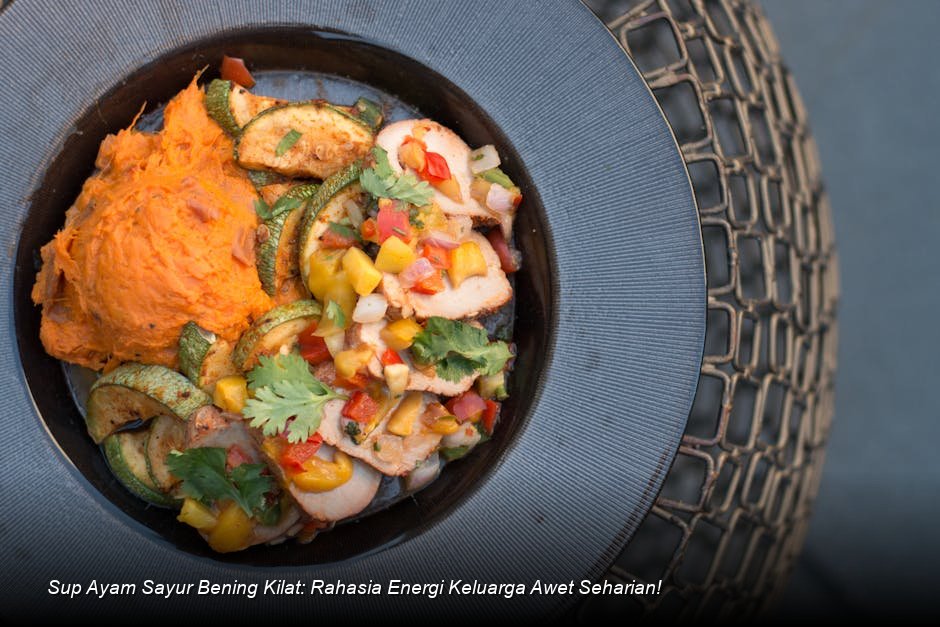 Semangkuk penuh Sup Ayam Sayur Bening yang jernih dengan irisan wortel oranye cerah, taburan daun bawang segar, disajikan di atas meja kayu.