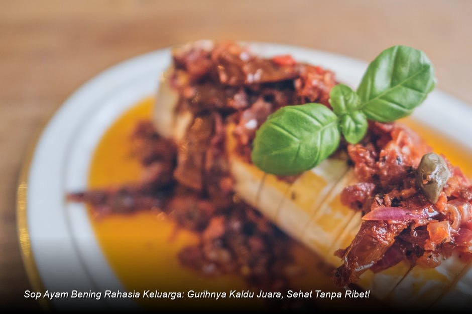 Semangkuk besar Sop Ayam Bening yang jernih, menampilkan potongan wortel oranye cerah, ayam empuk, dan taburan daun bawang segar sebagai garnish.